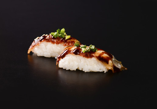 Nigiri sushi à l'anguille glacée, garni de ciboulette sur fond noir