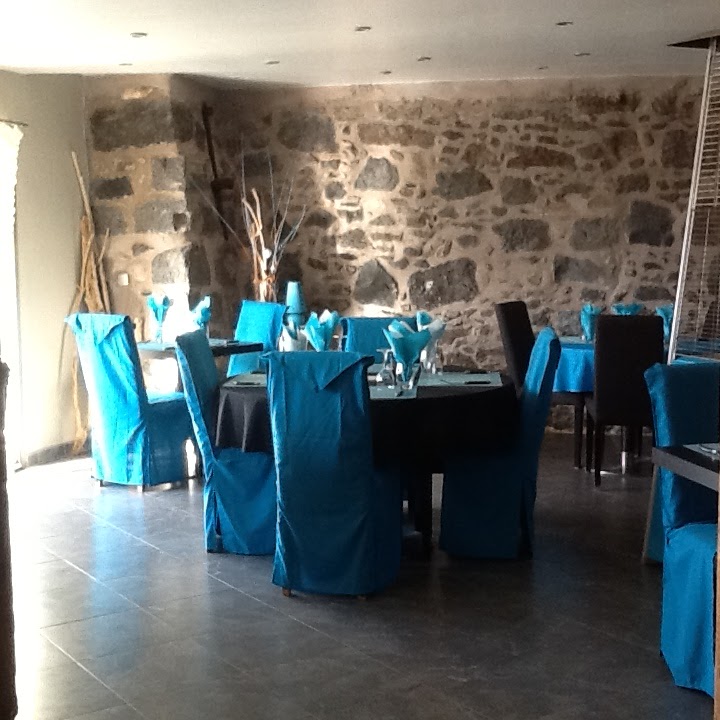 Salle intérieure du restaurant avec mur en pierre et chaises turquoise