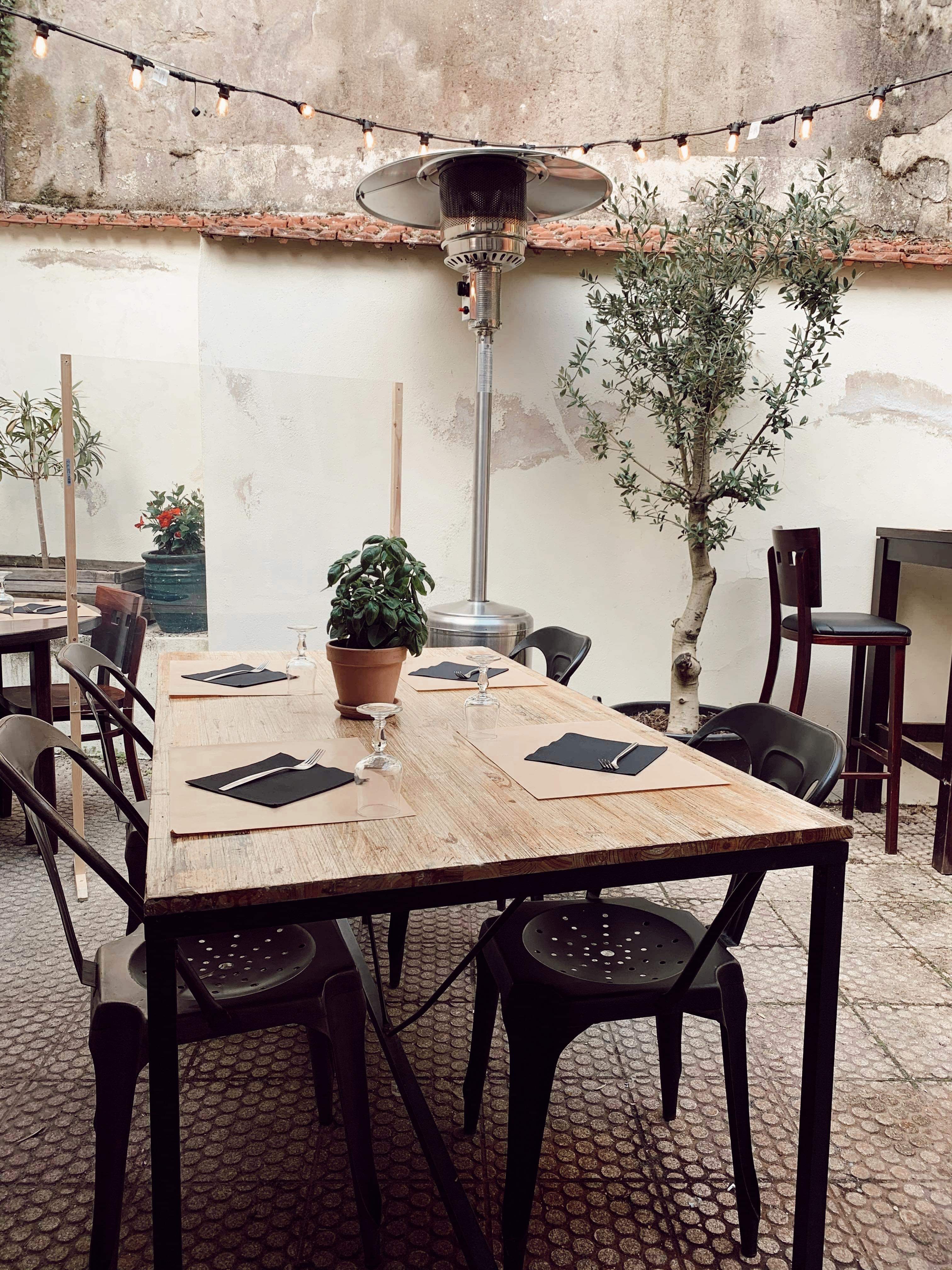 Terrasse extérieure avec guirlandes lumineuses, olivier et tables en bois dressées