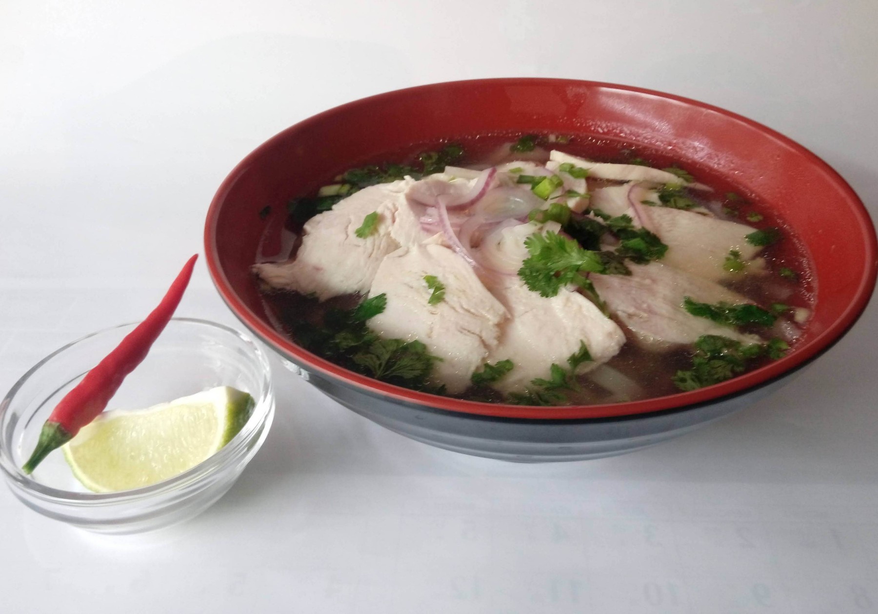 Phở au poulet avec bouillon clair, herbes fraîches, citron vert et piment