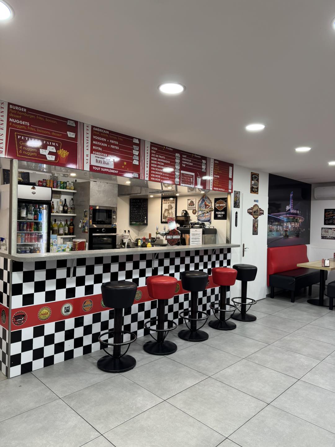 Intérieur rétro du Snack Bar Jacqueray avec comptoir à damier noir et blanc, tabourets rouges et noirs, et tableaux de menu